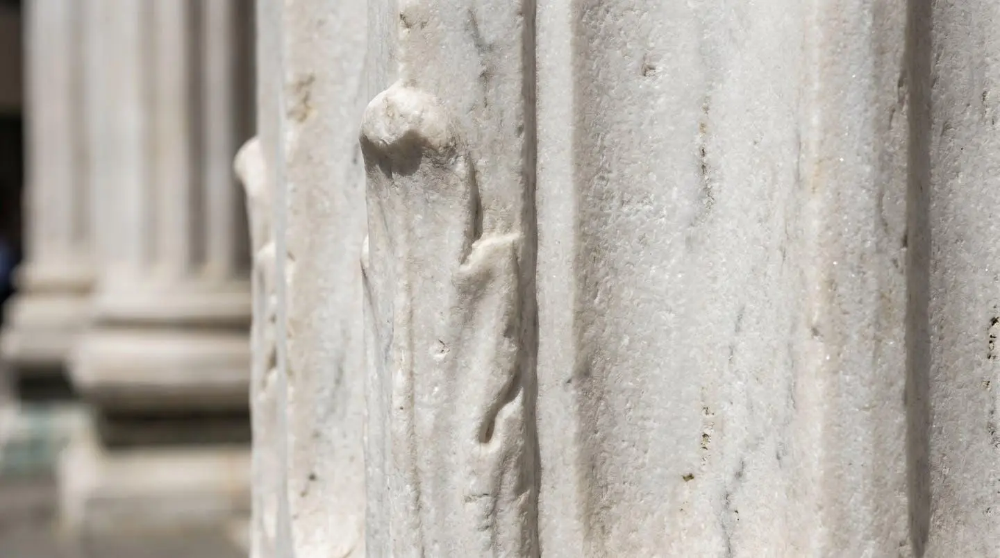 Extreme close-up of white marble columns and carved stone architectural detail from a historic Tuscan monument, shallow depth of field with blurred background